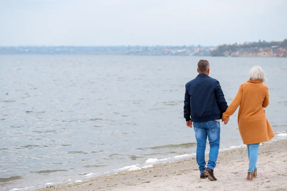 An older couple walking together along the shoreline