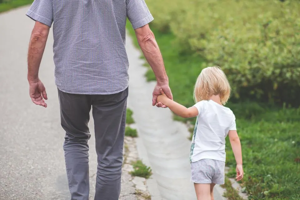A parent and young child walking hand in hand on a garden path